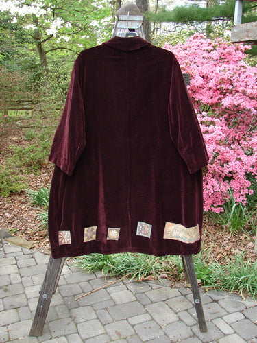 1999 Patched Velveteen Poet's Coat Holiday Deep Burgundy Size 1 displayed on a stand, featuring oversized vintage buttons, a wrapped folded collar, and colorful holiday Celtic patches.