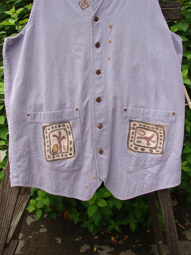 1996 Denim Visionary Vest Travel Stone Stratus Size 1: A light blue denim vest with a V-shaped neckline, metal front buttons, and rivet-topped pockets. It features a rear buckle draw tab, a shirt tail front hem, and an upward scooped back line. The vest is adorned with a travel-themed paint design.