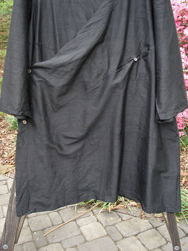 2000 Shaunting Silk Slant Wrap Jacket Unpainted Deep Black Size 2 displayed on a wooden frame outdoors, featuring textured fabric, wide sleeves, buttons, and a slanted gathered seam for a vintage, expressive style.