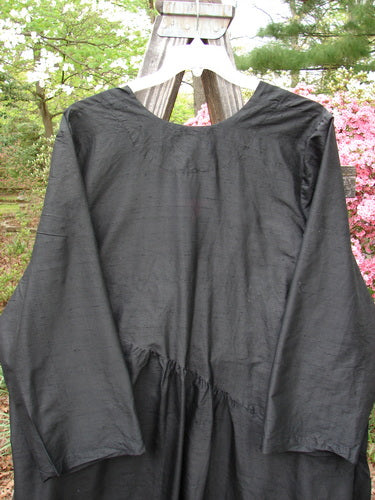 2000 Shaunting Silk Slant Wrap Jacket Unpainted Deep Black Size 2, displayed outdoors on a wooden hanger, highlights its billowy, slightly shimmery fabric with wider rounded sleeves and classic diagonal slit pockets.