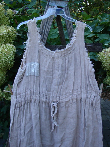 Magnolia Pearl Heavy Gauze Embroidered Signature Farm Love Overall Natural OSFA displayed outdoors, featuring a loose fit, sleeveless design, drawstring waist, and lace-trimmed neckline, hanging against a floral backdrop.