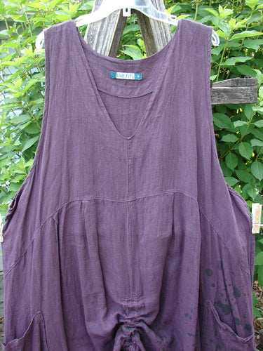 Barclay Linen Two Pocket Pull Up Jumper Berry Vine Red Plum Size 2, showcasing a feminine A-line shape with vertical seams, softly dipped V-neckline, and dual pleats, draped over a wooden fence.