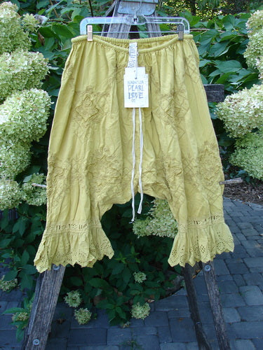 Magnolia Pearl NWT Embroidered Khloe Bloomer Golden Daffodil OSFA pants with scalloped lace ruffle, floral embroidery, drawstring waistband, and white Mantra Pearl Love hang-tag, set against a green backdrop.