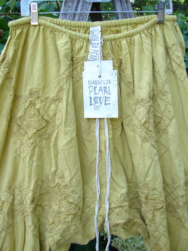 Magnolia Pearl NWT Embroidered Khloe Bloomer Golden Daffodil OSFA, showcasing bohemian harem-style, features intricate floral embroidery, flutter bottoms, and a drawstring waist, hanging with a signature Magnolia Pearl Love Co. tag.