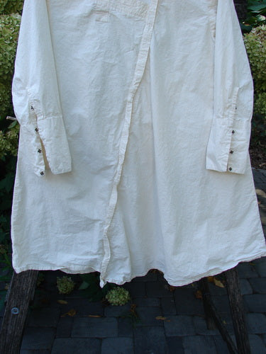 Magnolia Pearl Cotton Poplin Wabi Diagonal Tunic Natural OSFA displayed outdoors, featuring diagonal seams, long sleeves with buttoned cuffs, and a partially open front placket, draped over a wooden ladder.