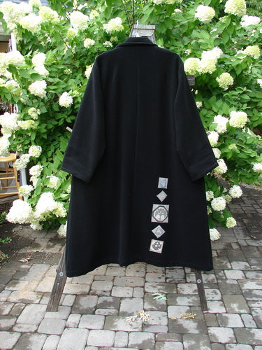 1999 Patched Woven Overcoat Black Size 2 displayed on a hanger, showcasing vintage-inspired design with hand-sewn patches, oversized buttons, and deep inseam pockets, emphasizing its swinging A-line shape and foldable lower sleeves.