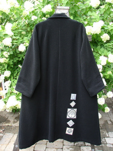 1999 Patched Woven Overcoat Black Size 2 displayed on a clothesline, featuring vintage-inspired design, hand blacked patches, oversized buttons, deep inseam pockets, and foldable sleeves.