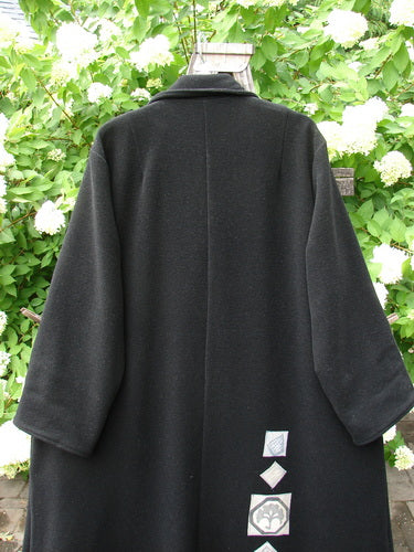 1999 Patched Woven Overcoat Black Size 2 displayed on a hanger, featuring hand-stitched patches, oversized buttons, deep pockets, and a swinging A-line shape with foldable sleeves.