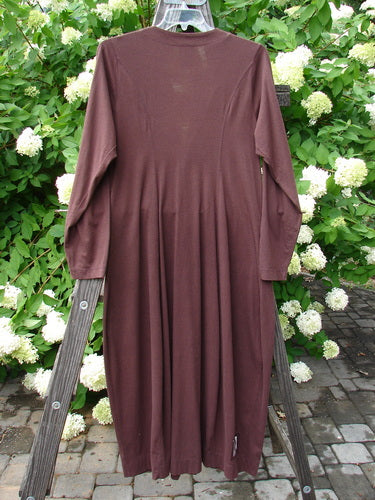 1998 Merino Pria Dress Unpainted Raisin Size 1, displayed hanging on a wooden rack, showcasing its long, hourglass shape with diamond-cut buttons, ribbed round neckline, and tapered sleeves.