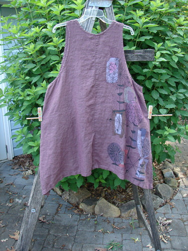 Barclay Linen Two Pocket Shirttail Pinafore Starburst Plum Wine Size 1 displayed on a wooden stand, highlighting its A-line flair, rounded neckline, and double drop exterior pockets.