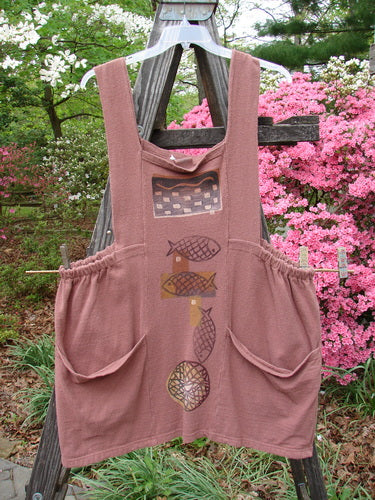 1995 Reprocessed Cottage Jumper Sea of Fish Clove Size 3 with fish design, thick shoulder straps, sectional bib, elastic sides, and large front pockets, hanging on a wooden pole.