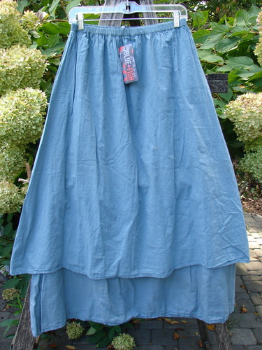 Barclay NWT Batiste Layer Skirt Unpainted Green Sea Size 0, features a lightweight, layered maxi style with an elastic waistband, displayed outdoors against a backdrop of leafy plants and hydrangeas.