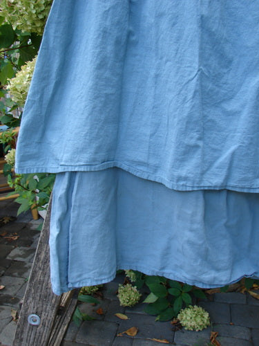 Barclay NWT Batiste Layer Skirt Unpainted Green Sea Size 0 draped on a wooden ladder, showcasing its lightweight, tiered design with a full elastic waistline and wide hem sweep in a garden setting.