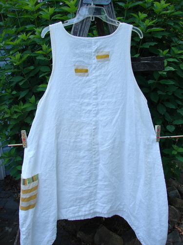 Barclay Linen Single Side Pocket Pinafore Geos White Size 1 displayed outdoors on a clothesline, showcasing its unique A-line flair, deeper arm openings, and distinctive exterior painted pocket.