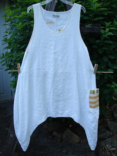 Barclay Linen Single Side Pocket Pinafore Geos White Size 1 hangs on a clothesline, showcasing its medium-weight linen, A-line flair, deep scoop neckline, and unique exterior painted pocket.