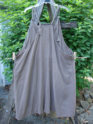 Barclay Linen Rayon Pucker Side Pocket Apron Jumper Unpainted Bark Size 1 displayed, showcasing adjustable shoulder straps, double front pockets, and a softly textured pucker rib, hanging on a clothesline.