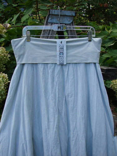 Barclay NWT Batiste Fold Over Raglan Silhouette Skirt Unpainted Dew Size 1, featuring a light-blue, full-skirted design with a wide fold-over waistband, displayed against a natural outdoor backdrop.