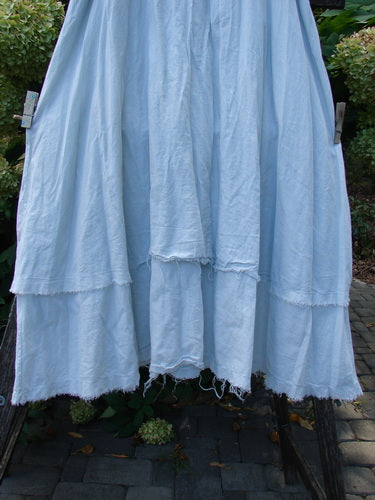 Barclay NWT Batiste Fold Over Raglan Silhouette Skirt Unpainted Dew Size 1, showcasing its light-blue, tiered layers with frayed hems, hangs outdoors, emphasizing its airy and generous two-tiered design.