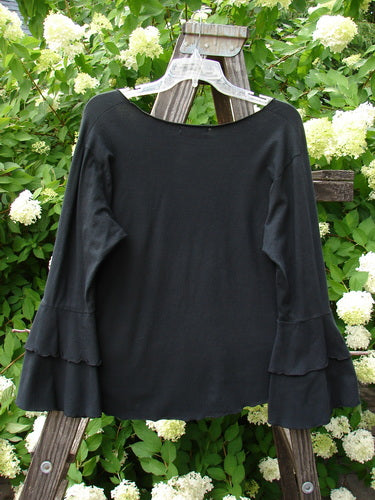 Barclay Cotton Lycra Long Sleeved Petal Top Unpainted Black Size 0 displayed on a wooden stand, showcasing its rounded raw neckline, fluttered lowers, and curly stitchery.