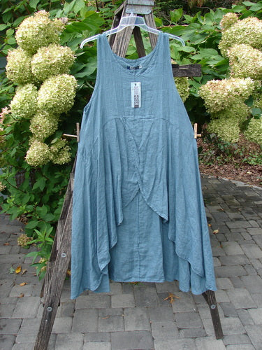 Barclay NWT Linen Tulip Midlayer Overpiece Unpainted La Mer Size 0 hangs on a ladder, showcasing its layered, draped front panel and open, sweeping A-line silhouette, emphasizing creative, individual expression.