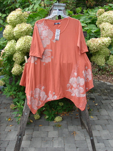 Barclay NWT Origami Tunic Top Berrie Patch Orange Cachi Size 0, features a loose, tunic-style fit with white floral motifs and raw edges, displayed on a wooden ladder amidst greenery.