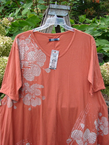 Barclay NWT Origami Tunic Top Berrie Patch Orange Cachi Size 0 features an oversized design with white floral graphics, an oval neckline, raw edges, and unique hemline, displayed against green foliage.