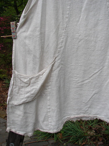 Barclay Slub High Vent Figure 8 Lace Pocket Pinafore Dress Unpainted Crème Size 2, hanging on a clothesline, showcasing its unique figure-eight seams, widening center panel, and pinched exterior pockets.