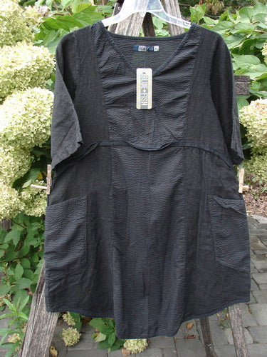 Barclay NWT Linen Pucker Heart and Soul Pocket Dress Unpainted Black Size 0, featuring a deep V-neck, short sleeves, and contrasting front patch pockets, displayed against flowering shrubs, showcasing its textured, A-line design.
