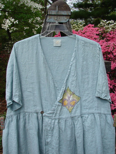 1999 Linen Adjustable Wrap Dress Butterfly Water OSFA displayed on a hanger, showcasing its adjustable crossover front, empire waistline, flouncy skirt, and butterfly print center wrap with pearl buttons.