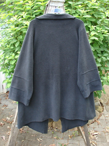 Barclay Celtic Moss Asymmetrical Collar Coat Unpainted Black Size 0, featuring a unique offset collar, three-button closure, varying hemline, belled sleeves, and a large exterior pocket, displayed on a clothes rack.