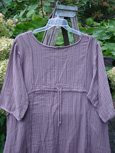 Barclay NWT Gauze Daily Pocket Dress Stripe Rose Earth Size 0, with three-quarter sleeves, vertical stripe texture, and unique rolled edgings, displayed on a hanger against a garden backdrop.