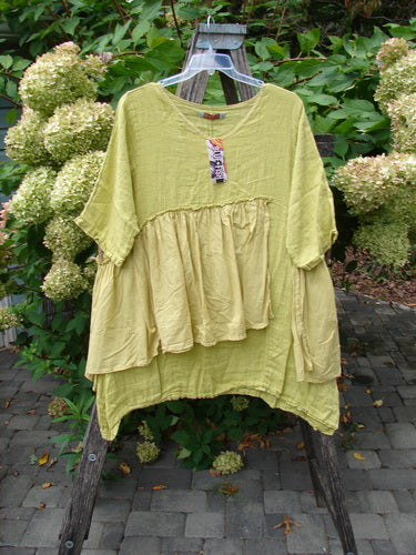 Barclay NWT Gauze Batiste Petal Urchin Flounce Dress Unpainted Citron Size 1, featuring a layered design with a gathered, two-tiered bodice and short sleeves, displayed on a wooden ladder outdoors.