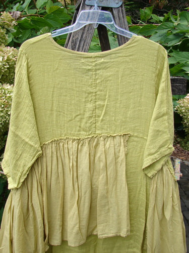 Barclay NWT Gauze Batiste Petal Urchin Flounce Dress in Citron, featuring a gathered waist and softly draped lower half, hangs on a clear hanger, showcasing its elegant, airy design.