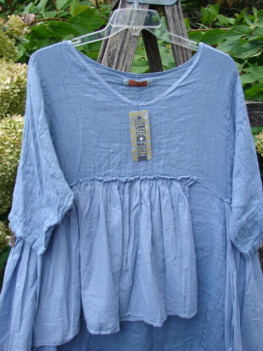 Barclay NWT Gauze Batiste Petal Urchin Flounce Dress Unpainted Dusty Sky Size 1, featuring a loose-fitting, sky-blue tunic with gathered empire waist, elbow-length sleeves, and a billowy bodice.