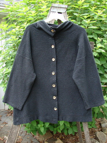 Barclay Crepe Mock Collar Jacket Unpainted Black Size 0 displayed on a wooden fence. Features a full button-up mock neckline, long wide sleeves, and drop shoulders with a heavy, slightly A-lined fall.