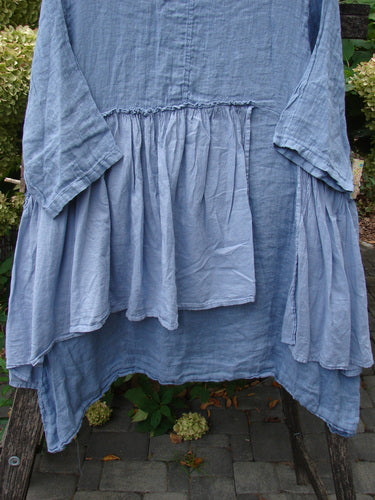 Barclay NWT Gauze Batiste Petal Urchin Flounce Dress in Dusty Sky, featuring a dropped waist and uneven hem, draped over a wooden bench outdoors, reflecting Bluefishfinder.com's vintage-inspired elegance.