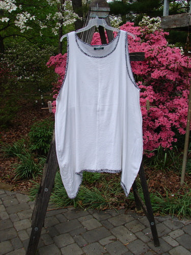 Barclay Crinkle Gauze Contrast Ditsy Daisy Pinafore Unpainted White Size 2 displayed on a clothes rack outdoors, showcasing its varying hem, scoop neckline, and full hem with floral accents.