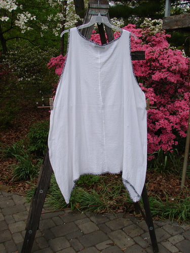 Barclay Crinkle Gauze Contrast Ditsy Daisy Pinafore Unpainted White Size 2 displayed on a wooden stand, highlighting its varying hem, scoop neckline, and full hem accented with a floral print.