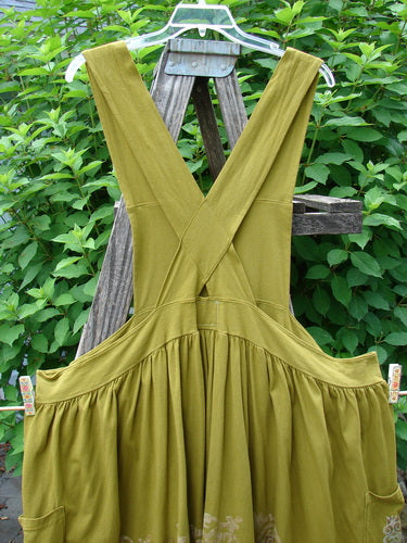 Barclay Overall Jumper Celtic Sun Glazed Tile OSFA displayed on a wooden stand, featuring a creatively cut bib, crisscross back straps, wide skirt, and oversized side wrap pockets.