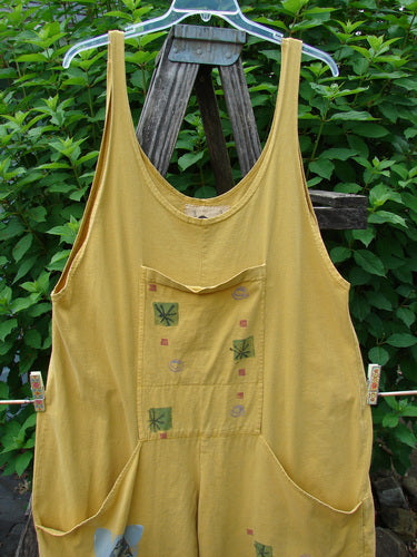 1991 Farmer Brown Overall Pant Jumper Vintage Fish Goldenrod OSFA displayed on a clothesline, showcasing its unique features like generous shoulder straps, dual stacked pocket, and extra lower leg panel.