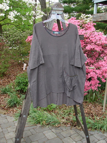 Barclay Gauze Contrast Ditsy Daisy Pocket Top Unpainted Stone Size 2 displayed on a wooden hanger, showcasing its wider neckline, exterior drop pocket with floral pattern, and drawcord back.