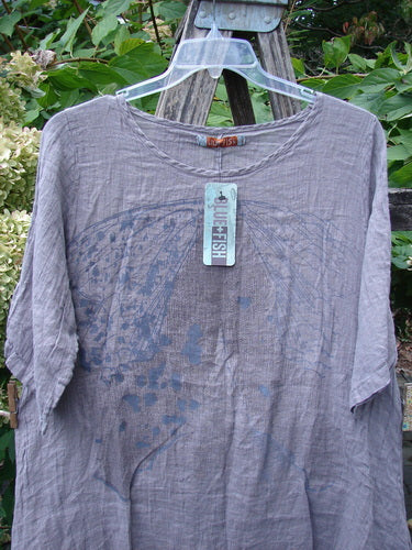 Barclay NWT Linen Simple Tunic Top Wing Mountain Opal Mauve Size 1 displayed on a hanger, featuring a scoop neckline, elbow-length sleeves, and an abstract graphic print against a garden backdrop.