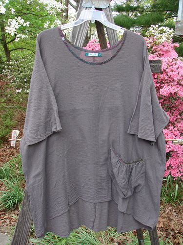 Barclay Gauze Contrast Ditsy Daisy Pocket Top Unpainted Stone Size 2 displayed on a wooden rack, featuring a wider neckline, exterior drop pocket, and drawcord back, showcasing a floral pattern.