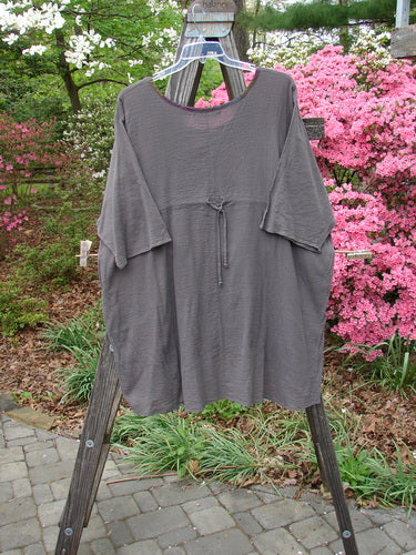 Barclay Gauze Contrast Ditsy Daisy Pocket Top Unpainted Stone Size 2 displayed on a wooden rack, showcasing a deeper and wider neckline with floral pattern and an exterior drop pocket.