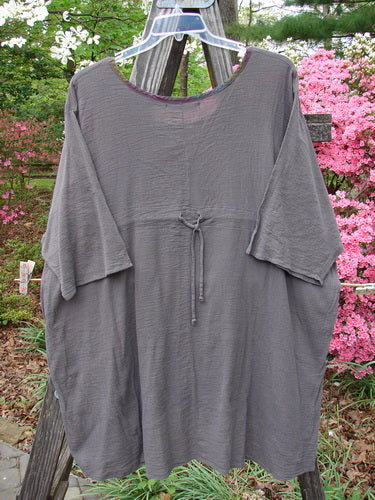 Barclay Gauze Contrast Ditsy Daisy Pocket Top Unpainted Stone Size 2 displayed on a wooden pole, showcasing a floral neckline and exterior drop pocket with a varying hemline.