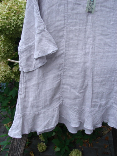 Barclay NWT Gauze Sectional Bias Flounce Top Unpainted Rice Paper Pink Size 1 draped outdoors, showcasing its lightweight linen with a flowy A-line shape, three-quarter sleeves, and banded flutter hem.