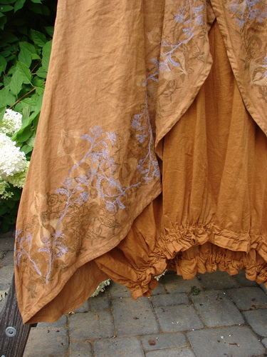 A close-up of the Barclay Linen Open Front Drawcord Hem Jumper in Squash, a dress with an interesting layered cross over front apron and batiste under skirt layer. The jumper features a downward curved empire waist seam, a deeper oval neckline, sectional rear panels, and an elastic gathered hemline. The dress is painted in the classic moving garden theme. Bust: 56, Waist: 58, Hips: 64. Length: 50 inches. Size 2.