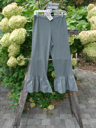 Barclay NWT Poplin Bottom Pantaloon Unpainted Chimera Size 0, featuring a wide ruffle hem, elastic waist, and cropped length, displayed on a wooden ladder in a lush garden setting.