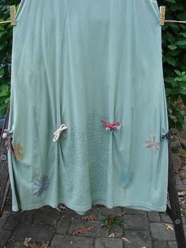 Barclay Constellation Jumper Garden Folly Aloe Size 1 displayed outdoors, featuring a deeply scooped neckline, pointed hemline accents, and a garden folly theme with sectional vertical panels, hanging on a clothesline.