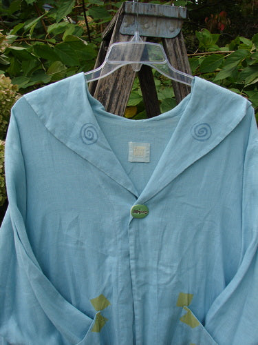 1999 Linen Breeze Jacket Tea & Cherries Spring OSFA, featuring spiral embroidery on lapels, a single button, patch pockets, and a sailor collar, draped on a wooden stepladder against a leafy background.